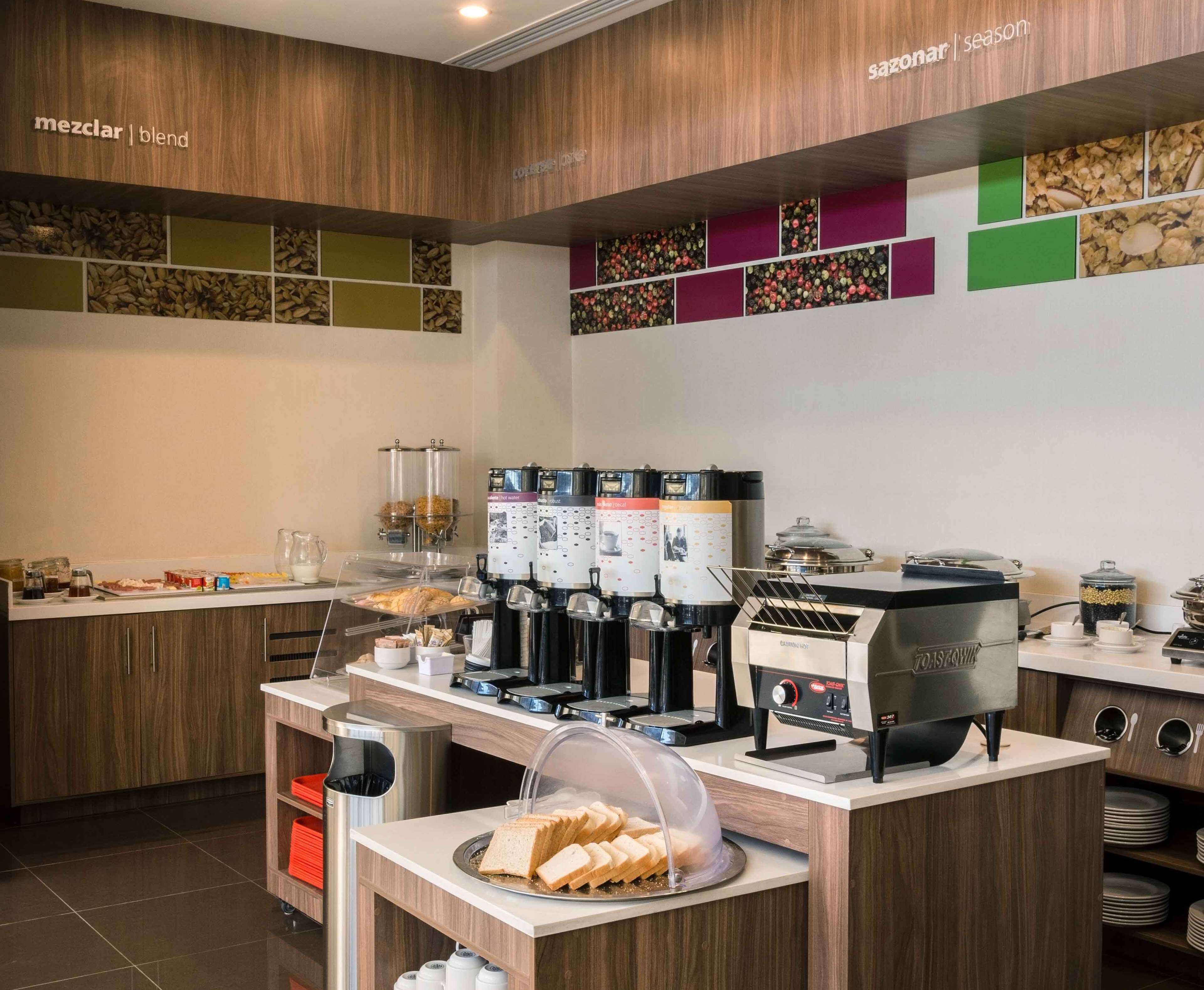 A modern breakfast bar with coffee machines, a bread display, and a variety of condiments.