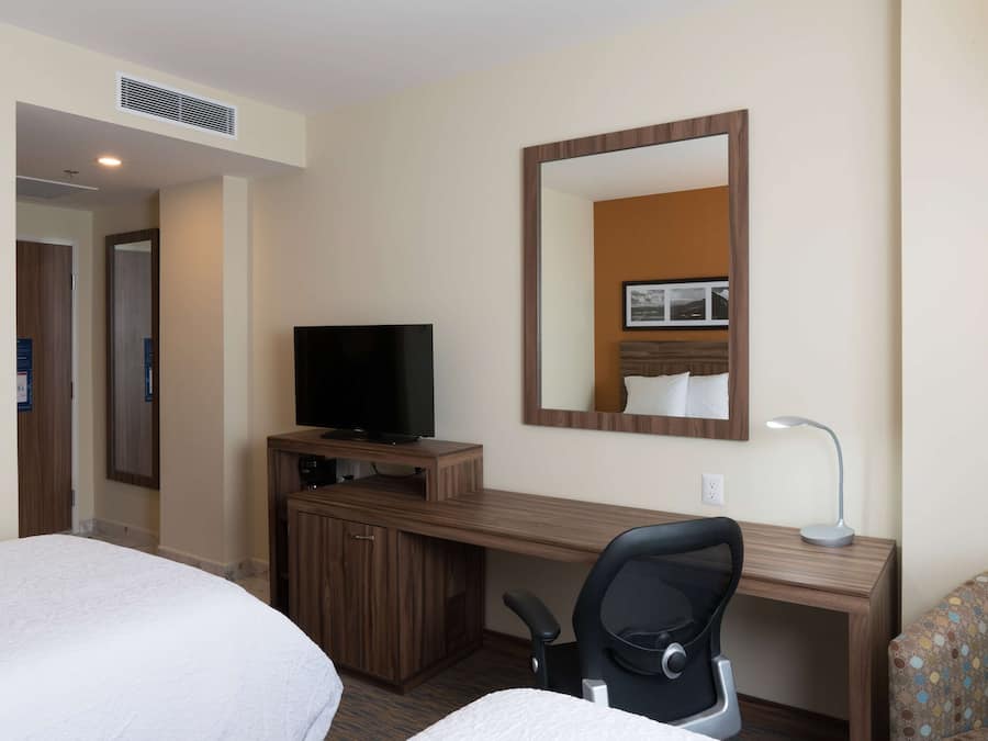 A hotel room with a bed, a desk with a television, a chair, and a large mirror.