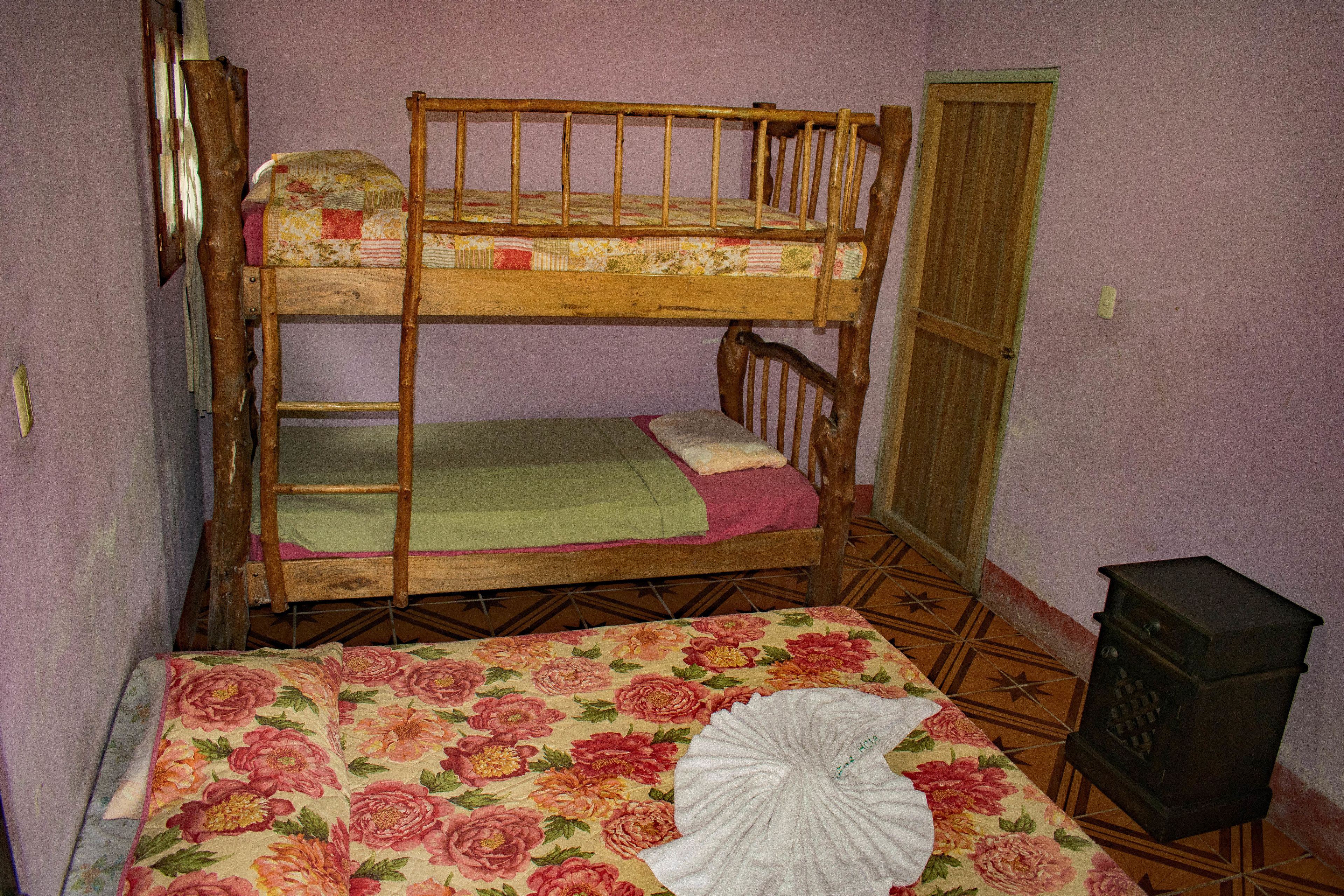 Una cama individual con colcha estampada, una mesita de noche de madera y una puerta en una habitación con paredes moradas.