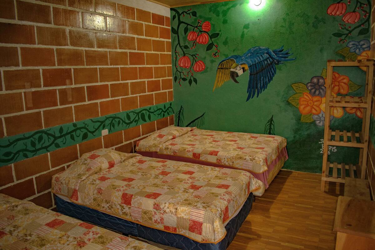 Una habitación con dos camas, una pared de ladrillo y un mural con un pájaro y flores.