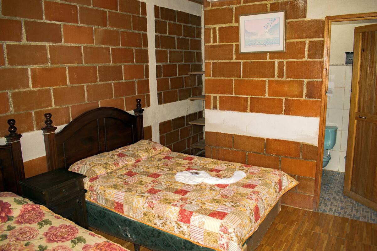 Un dormitorio con pared de ladrillo, estructura de cama de madera, colcha y mesita de noche de madera.