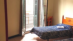 A room with two beds, a wooden chair, and a balcony with a metal railing. - Hostal Nilo (Barcelona)
