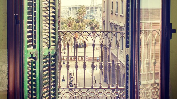 A view from a balcony with a metal railing and a glass door, overlooking a street with buildings and palm trees. - Hostal Nilo (Barcelona)