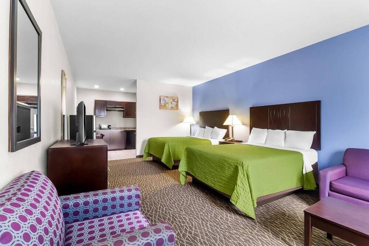 A hotel room with two beds, a sofa, a TV, and a kitchenette.