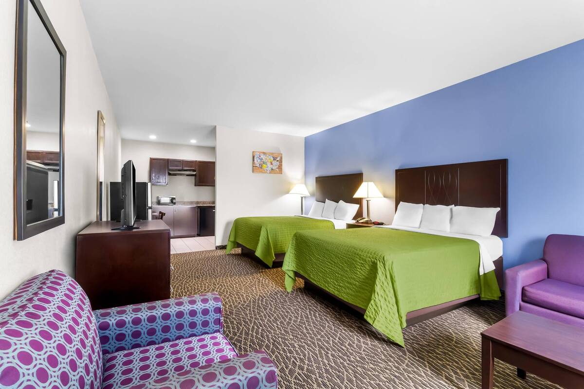 A hotel room with two beds, a sofa, a TV, and a desk.