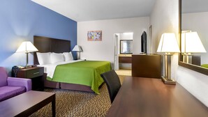 Una habitación de hotel con cama, escritorio, silla, sofá, lámpara y espejo.