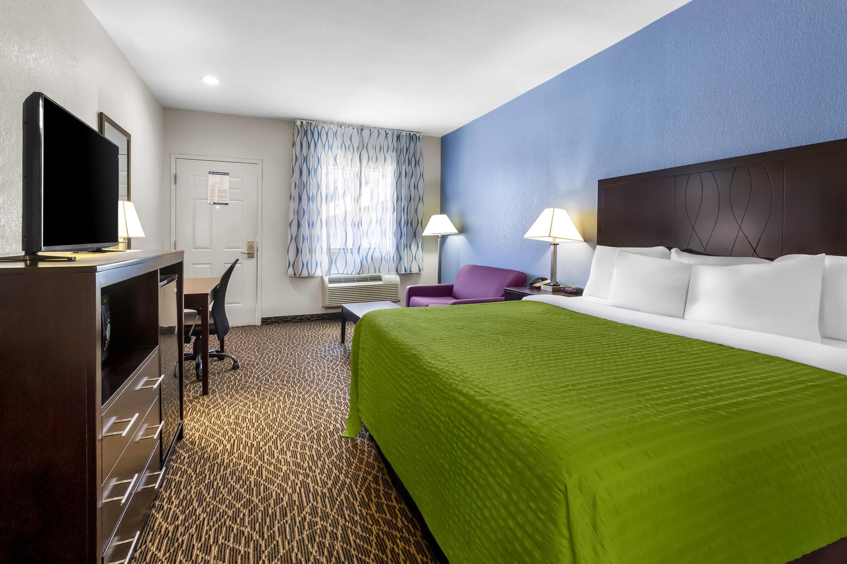 A hotel room with a bed, a desk with a TV, a chair, and a window with curtains.