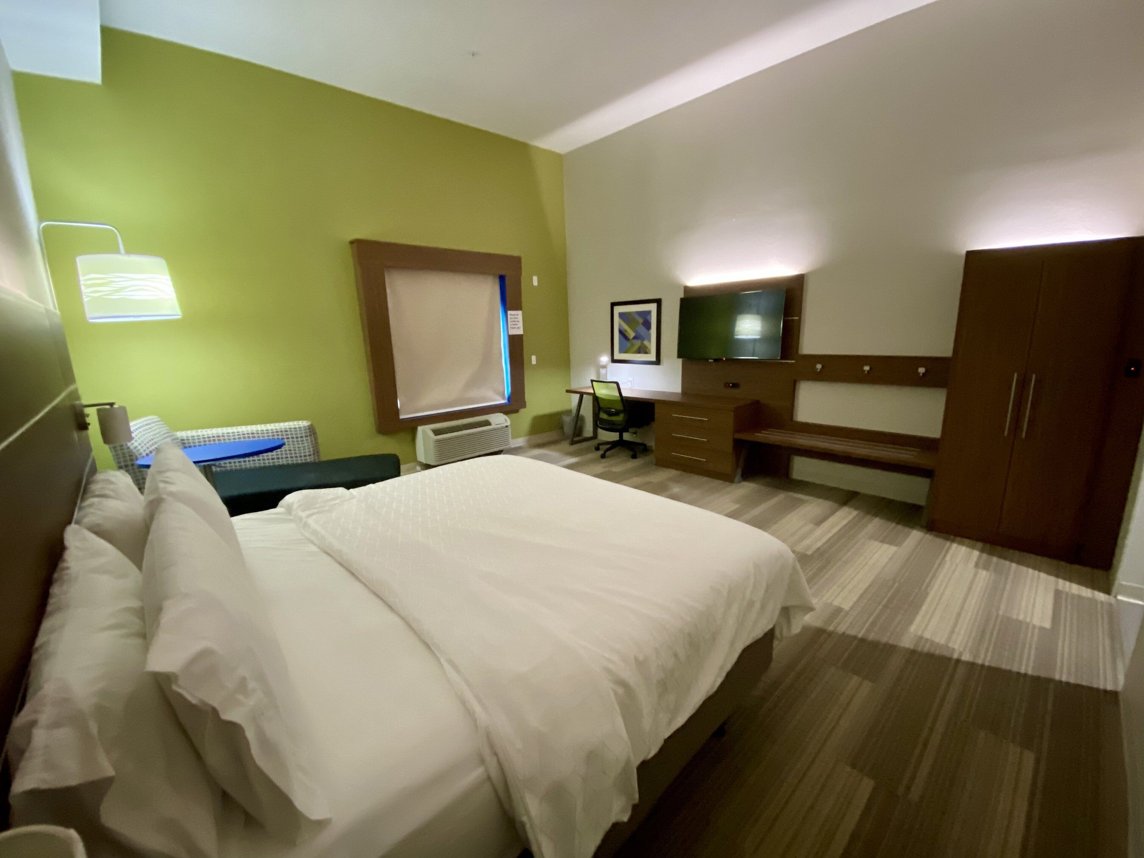 Una habitación de hotel con cama, escritorio, silla, televisor y armario.