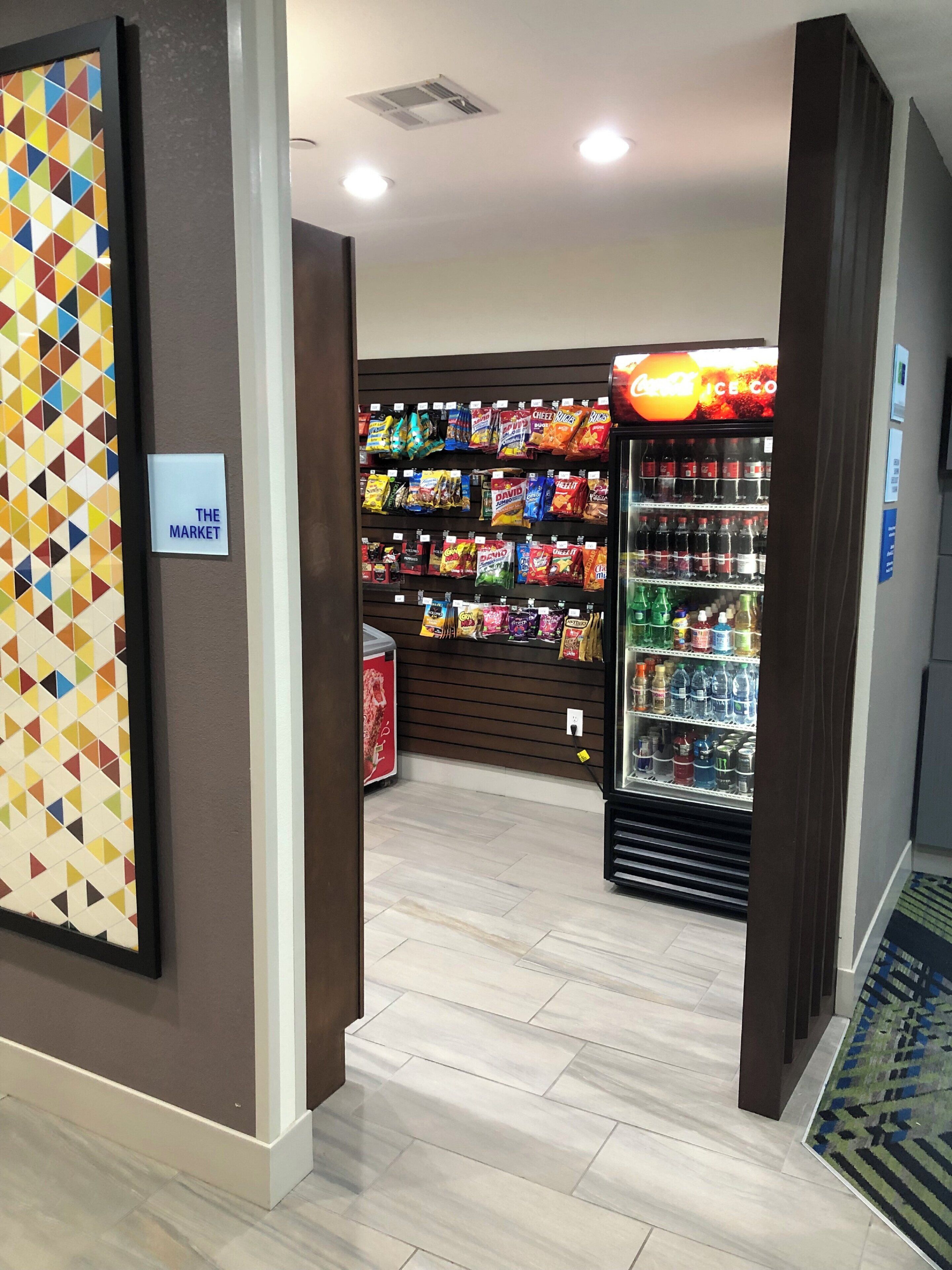 A hallway with a vending machine stocked with snacks and beverages, a sign labeled 'THE MARKET', and a patterned wall.