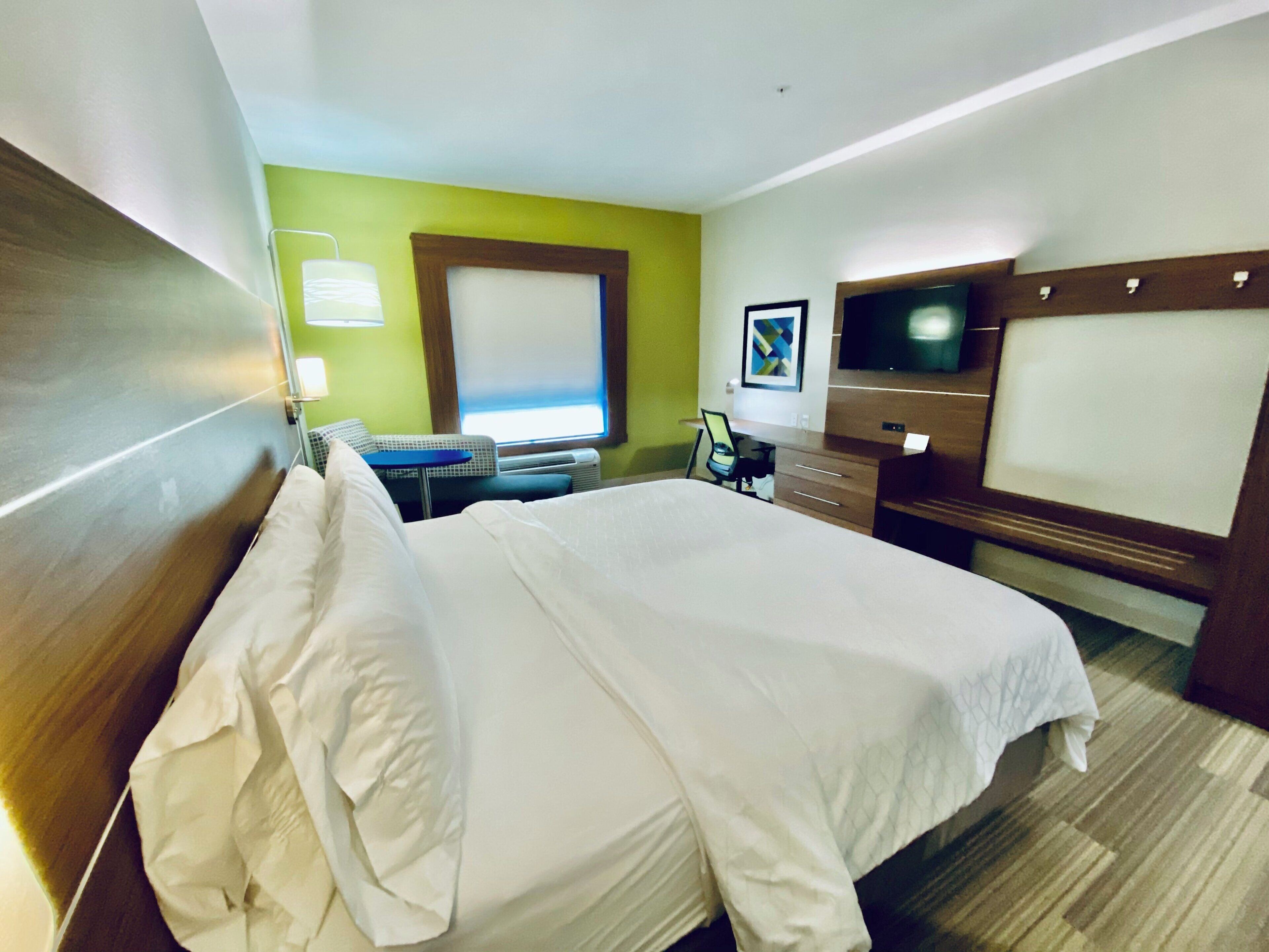 A hotel room with a large bed, a desk, a chair, a television, and a window with blinds.