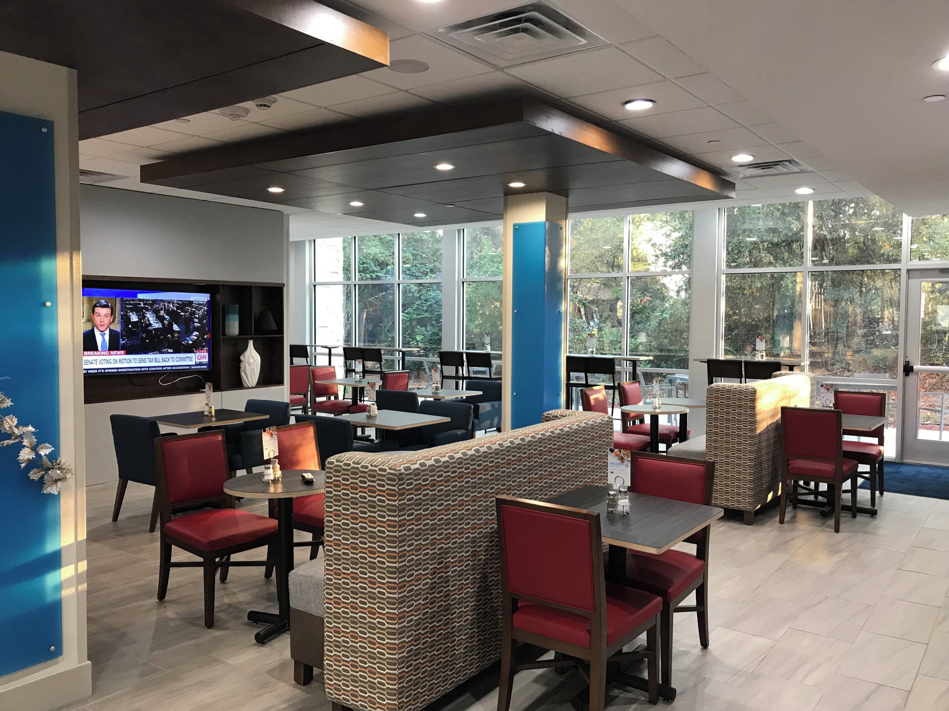 A restaurant with high ceilings, large windows, and a television displaying news.