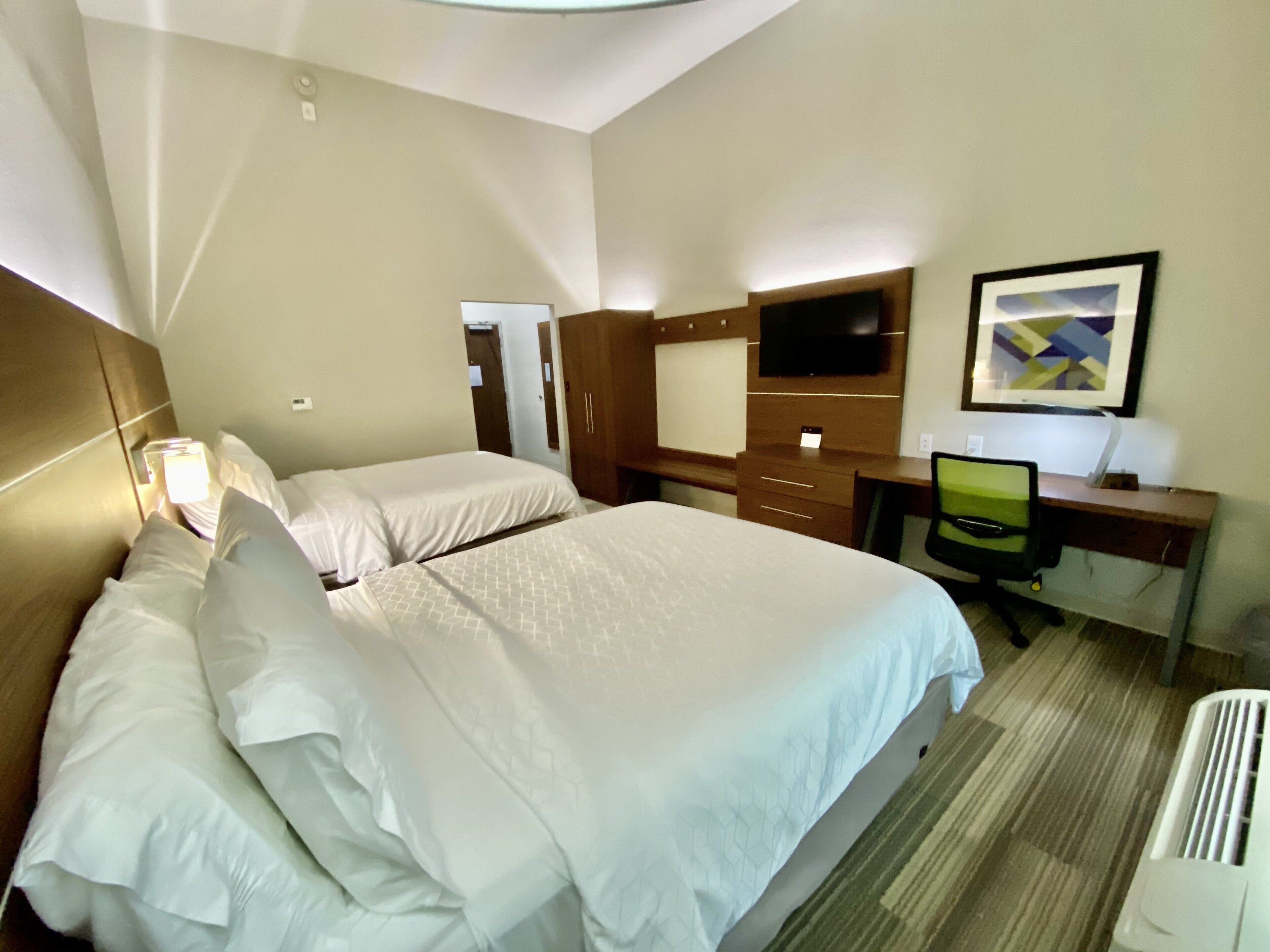 Habitación de hotel con dos camas, un escritorio, una silla, un televisor y un cuadro en la pared.