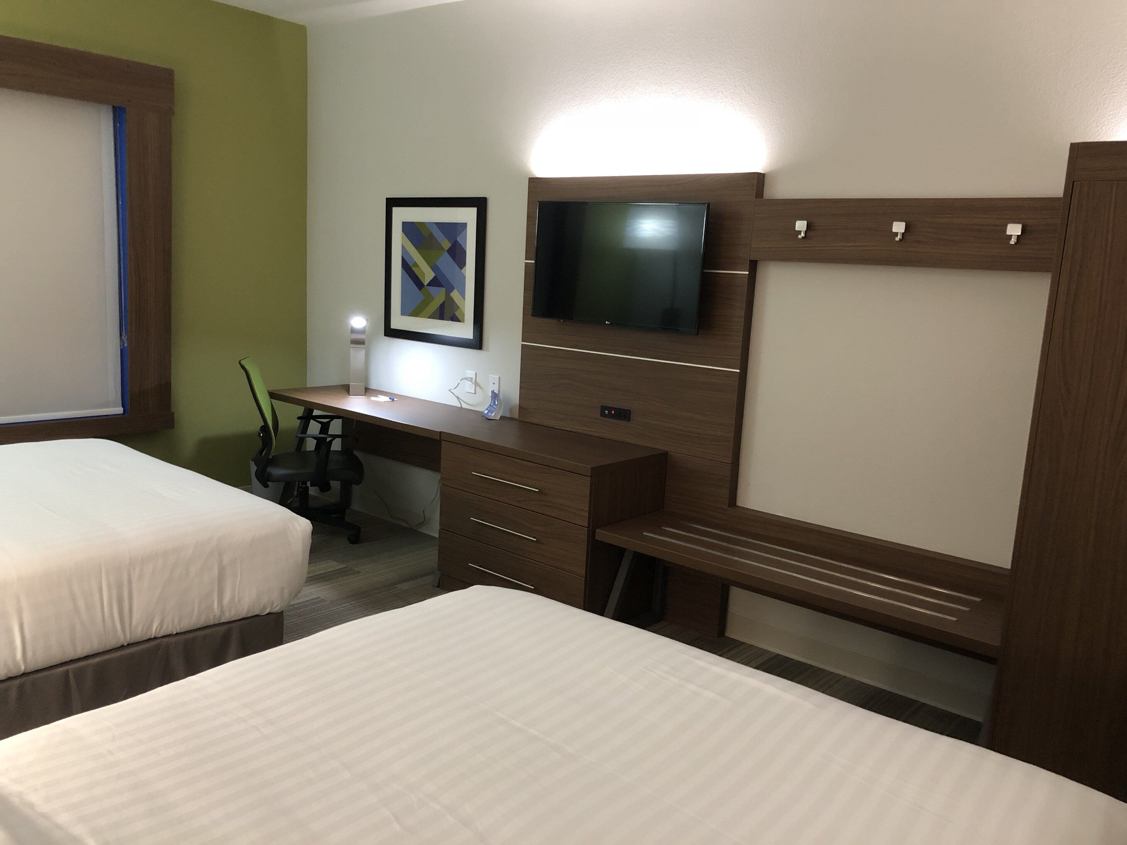 A hotel room with two beds, a desk with a computer, a television, and a framed picture on the wall.