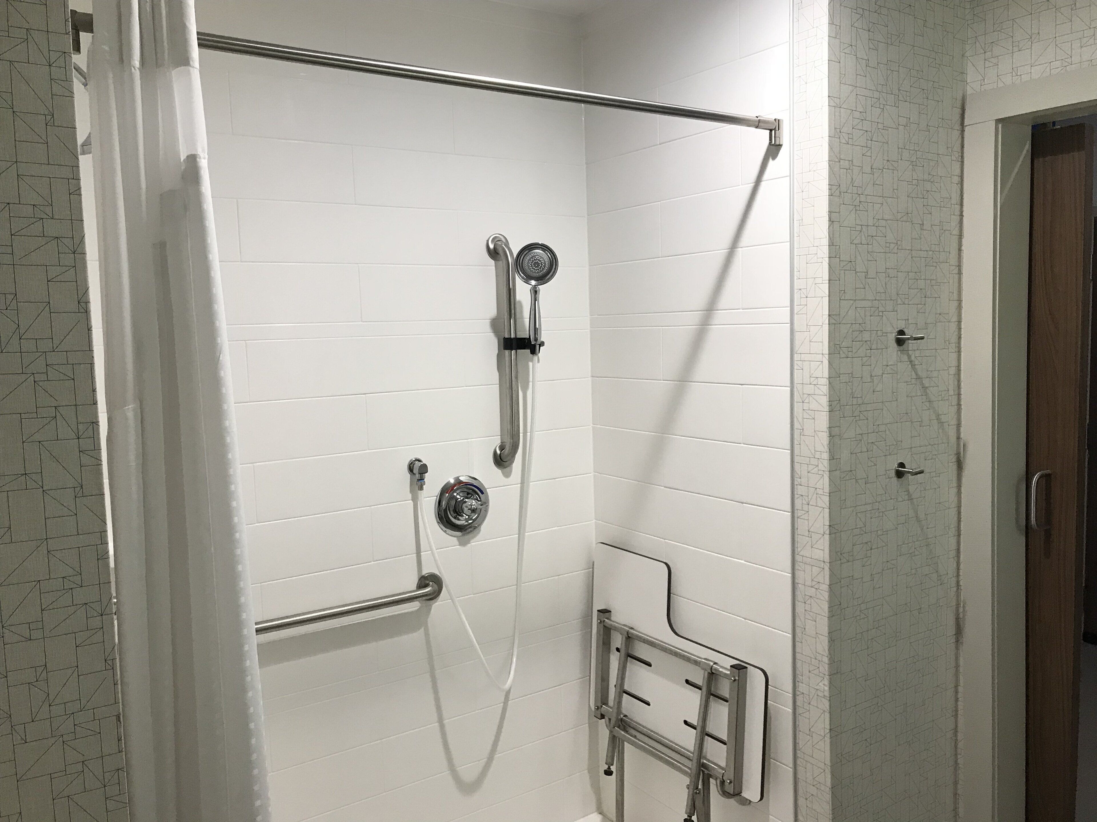 A shower with a handrail, a handheld showerhead, and a wall-mounted faucet.