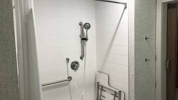 A shower with a handrail, a handheld showerhead, and a wall-mounted faucet.