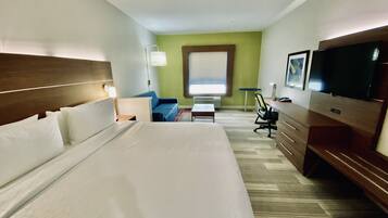 A hotel room with a large bed, a desk, a chair, a television, and a window.