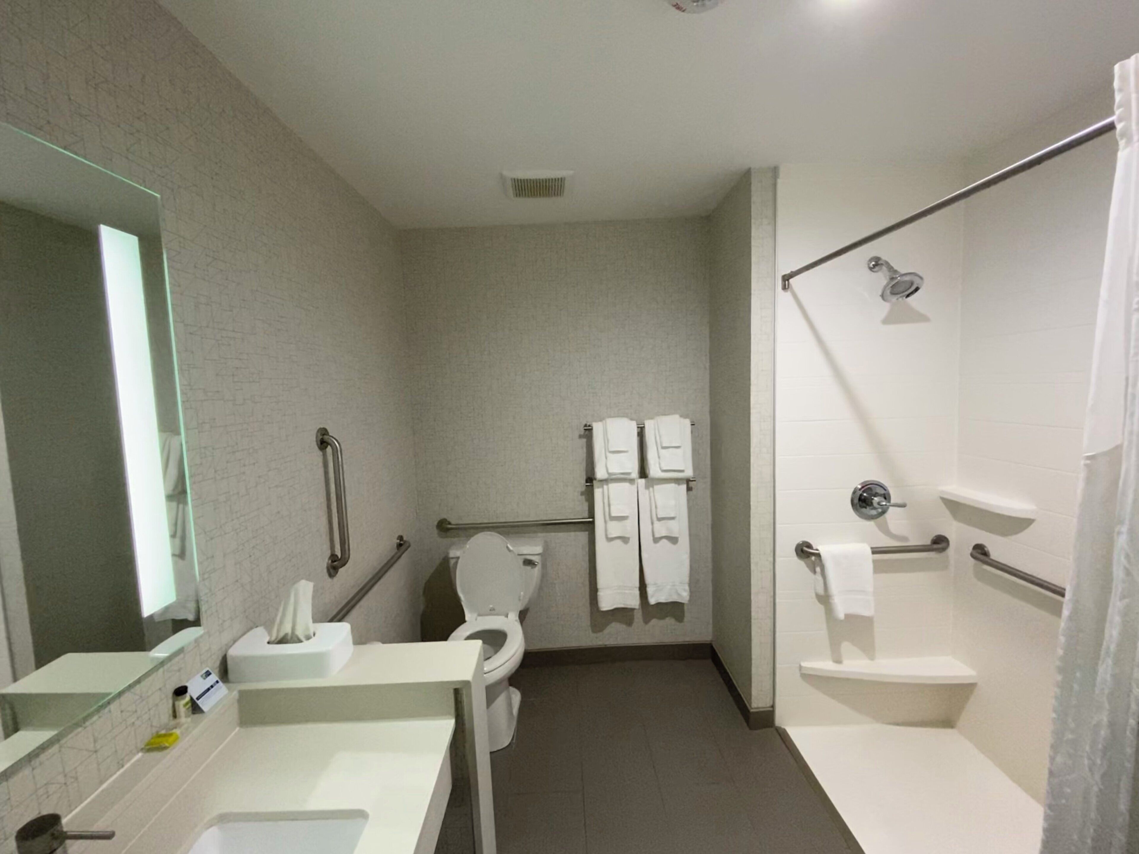 A bathroom with a toilet, sink, mirror, and shower area.
