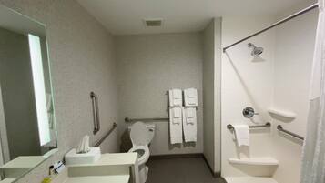 A bathroom with a toilet, sink, mirror, and shower area.
