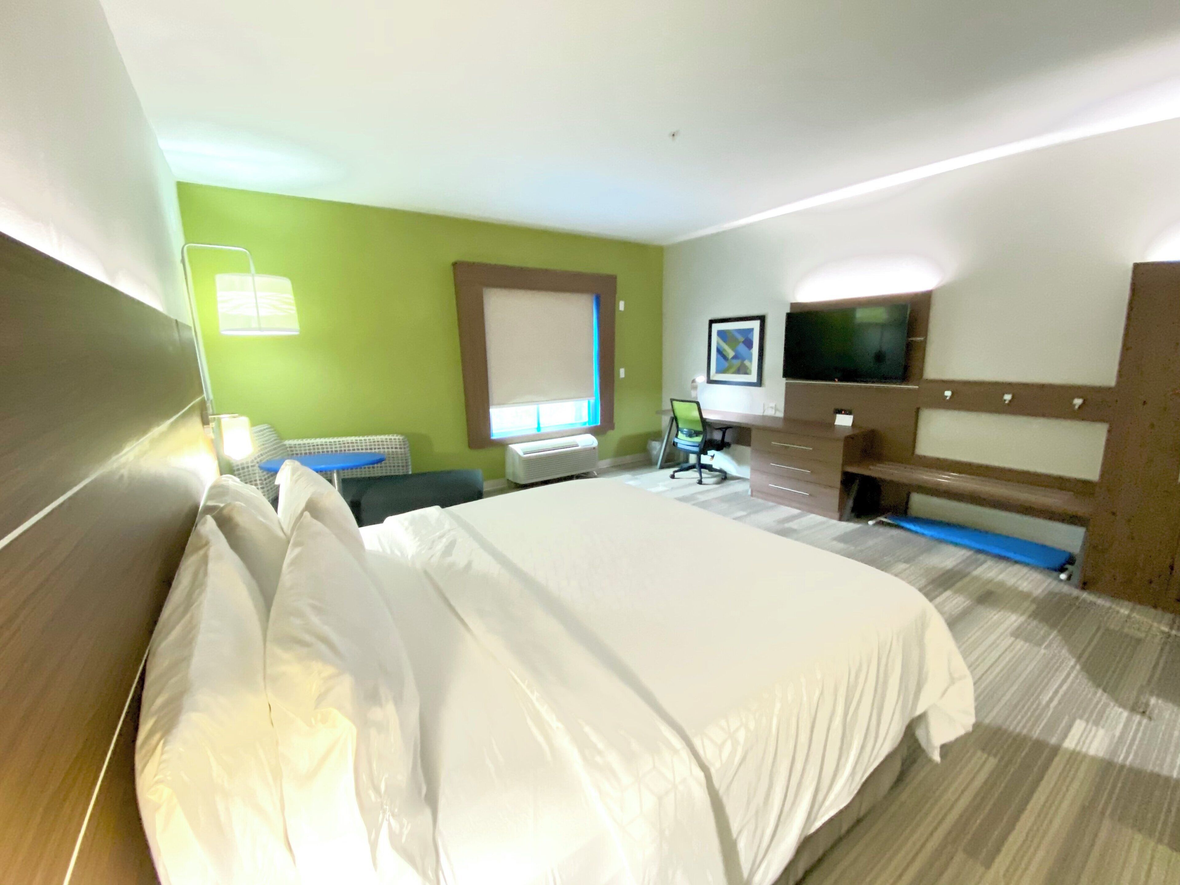 Habitación de hotel con una cama grande, un escritorio, una silla, un televisor y una ventana con persianas.