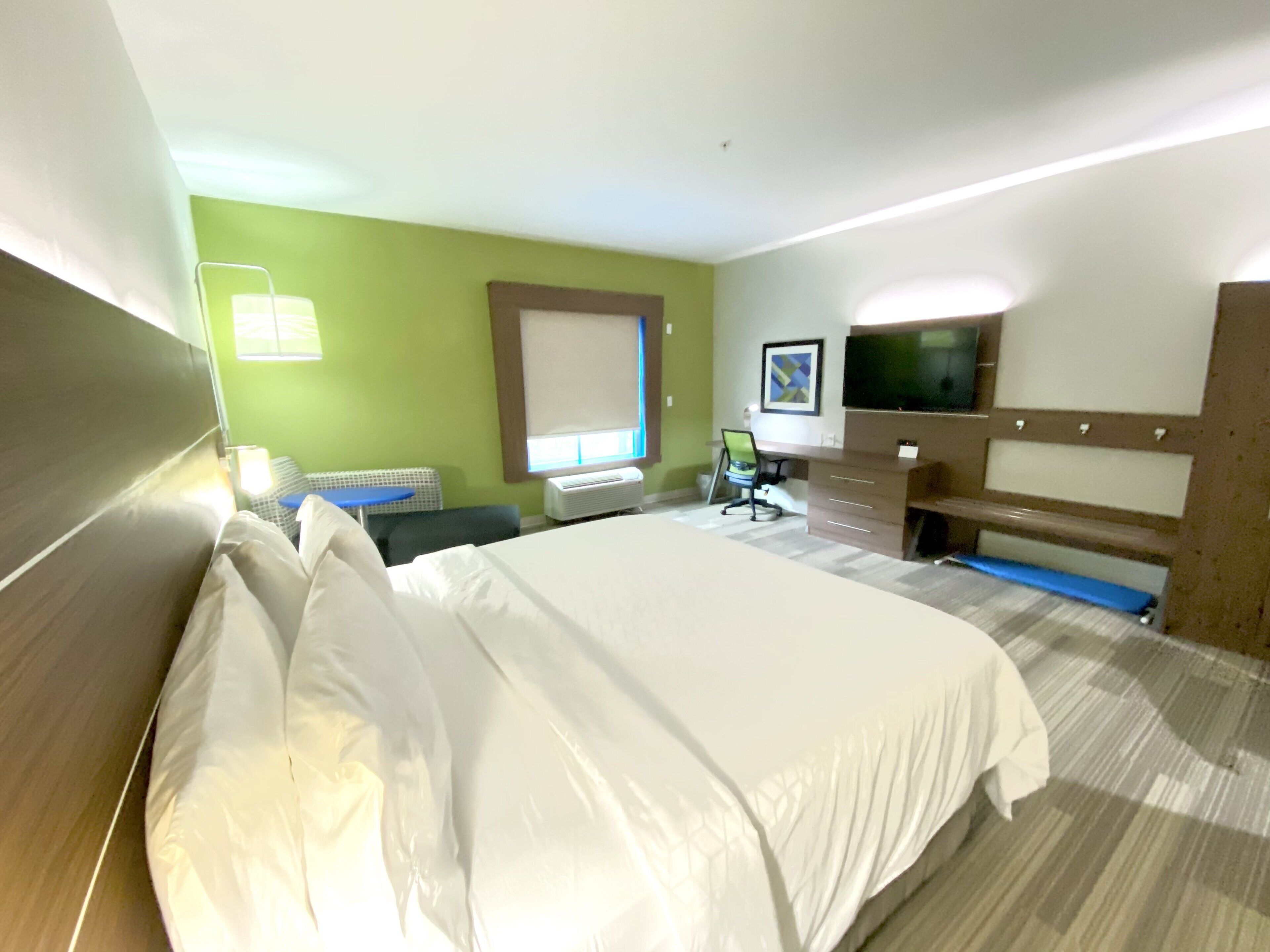 A hotel room with a large bed, a desk, a chair, a TV, and a window.