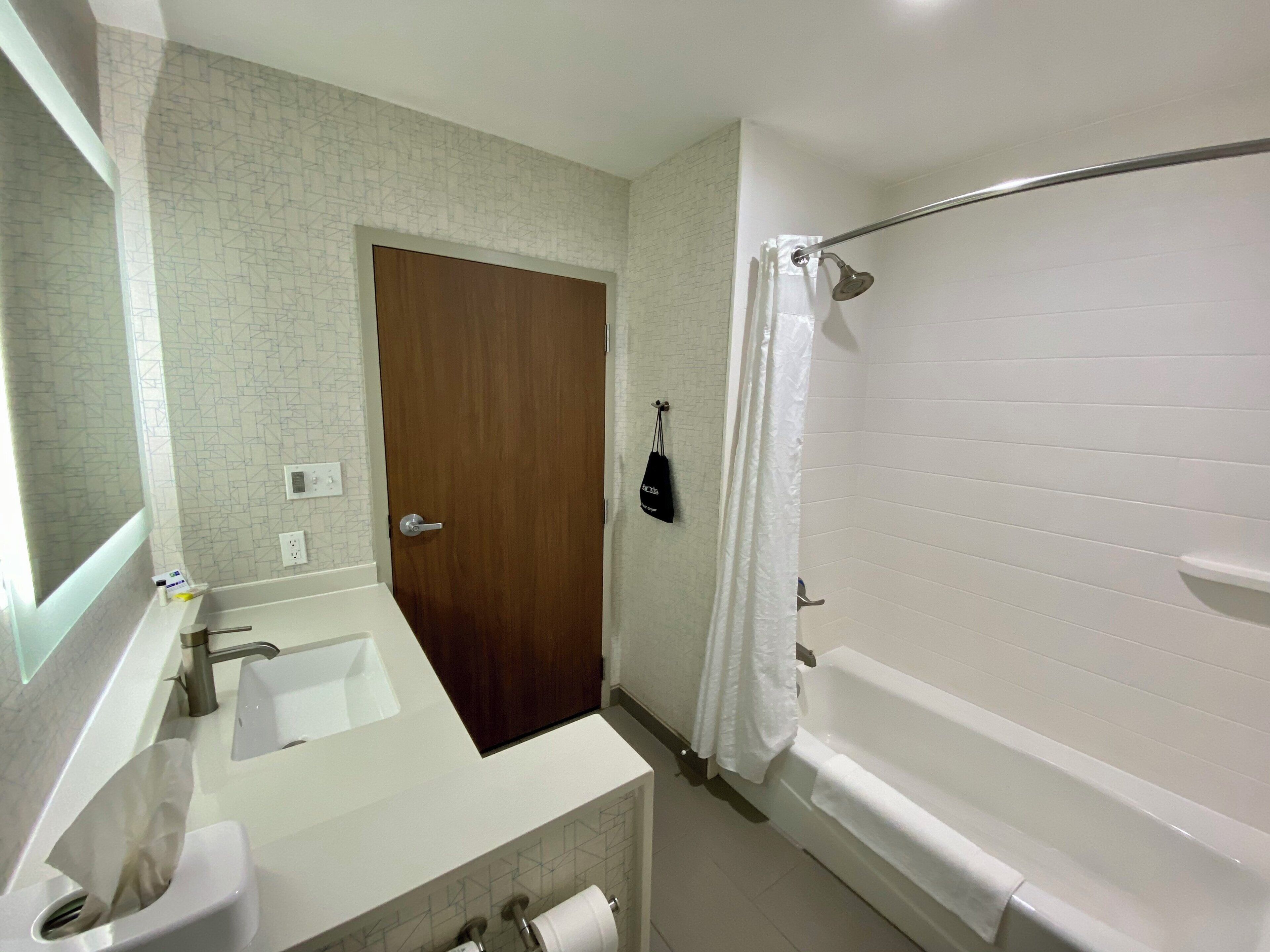 Un bany amb una porta de fusta, una banyera blanca i un lavabo amb mirall.
