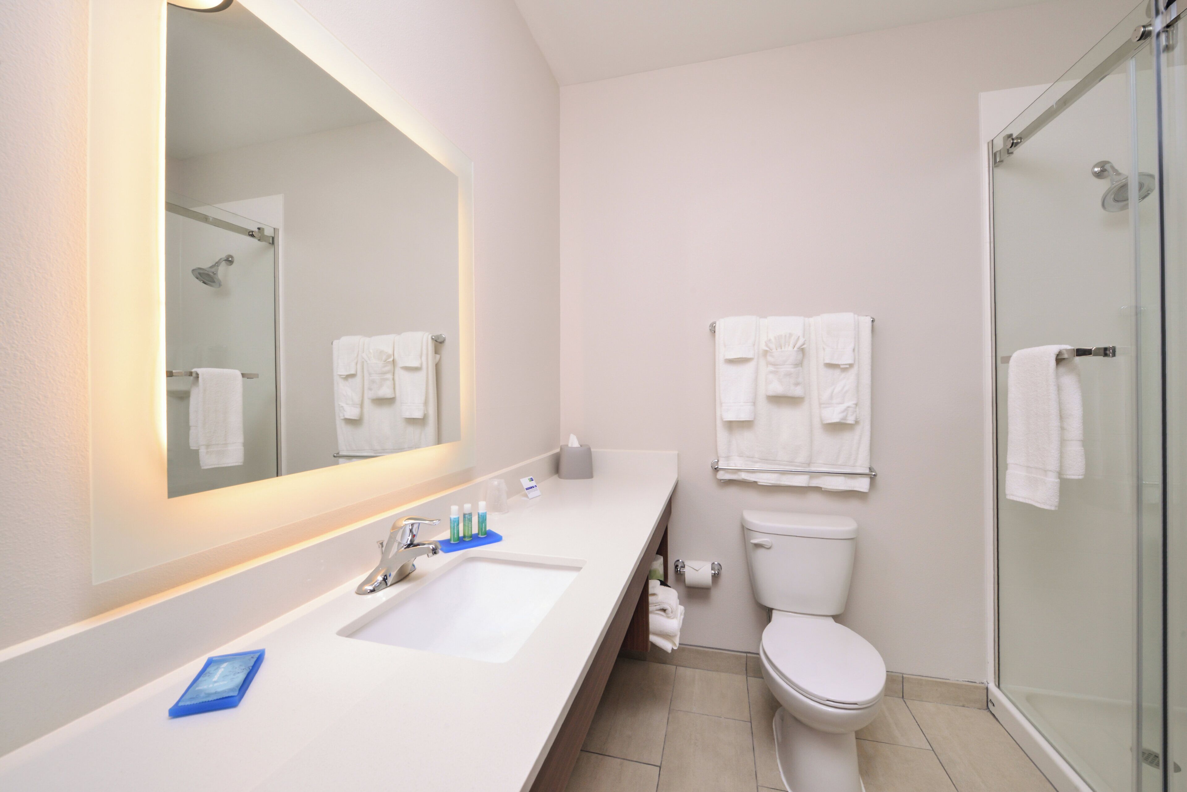 A modern bathroom with a large mirror, a sink, a toilet, and a glass shower enclosure.