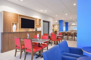 A modern restaurant interior with wooden paneling, red and blue seating, and a flat-screen TV mounted on the wall. - Holiday Inn Express Donaldsonville by IHG (Donaldsonville)