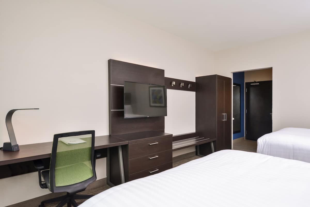 A hotel room with a desk, chair, TV, wardrobe, and two beds.
