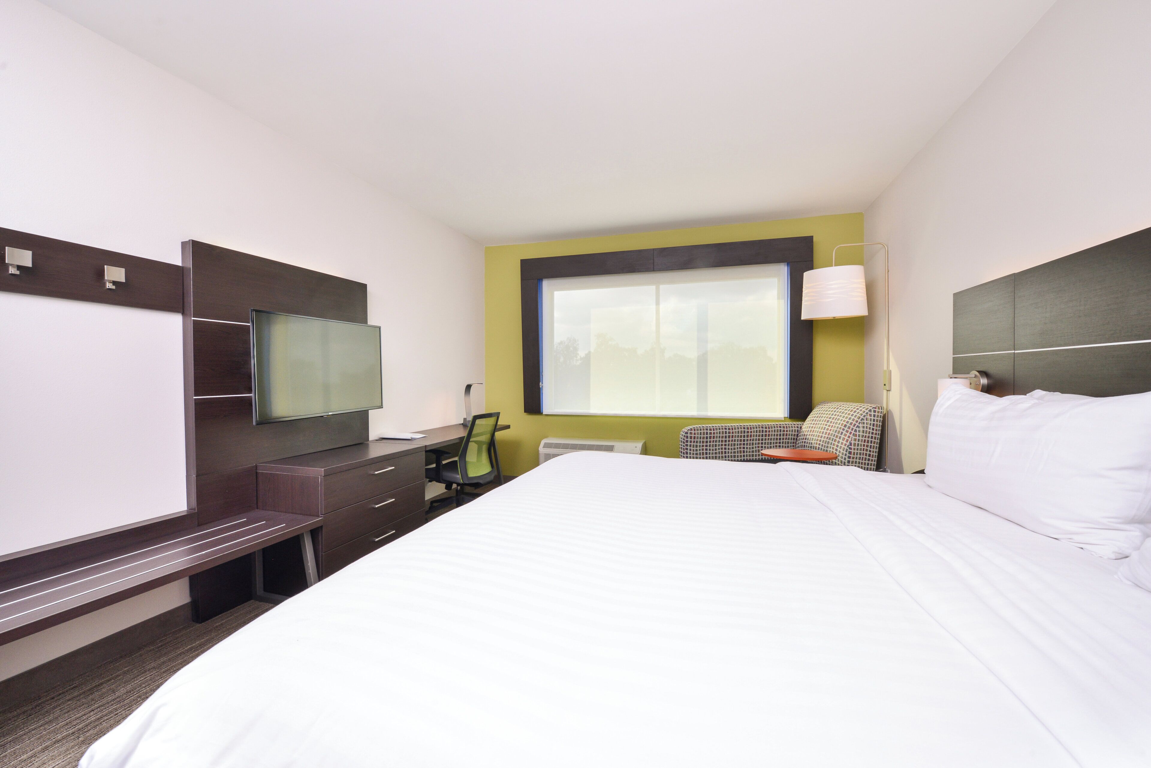 Una camera d'albergo con un letto, una scrivania, una sedia, una televisione e una finestra.