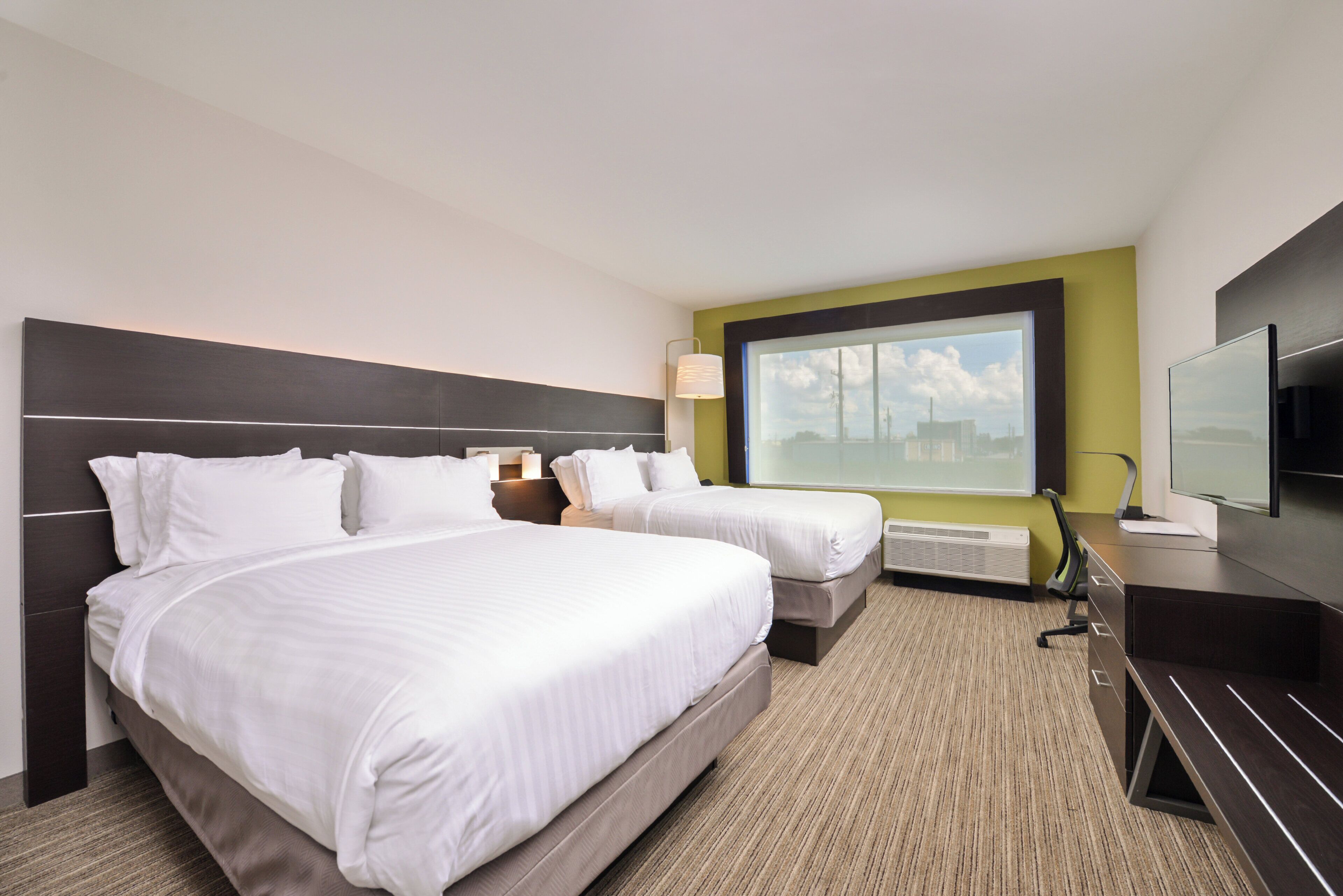 A hotel room with two beds, a large window with a city view, a flat-screen TV, and a desk with a chair.