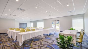 A conference room with multiple tables, chairs, and a large plant.