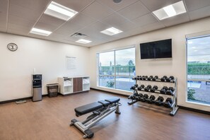 Et fitnesscenter med træningsudstyr, et tv ophængt på væggen og store vinduer.