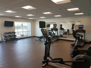 Ein Fitnessraum mit Laufbändern, Crosstrainern und einer Hantelbank.