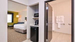 Une chambre d’hôtel comprenant un lit, un petit bureau avec un micro-ondes, une télévision et une salle de bain avec des serviettes.