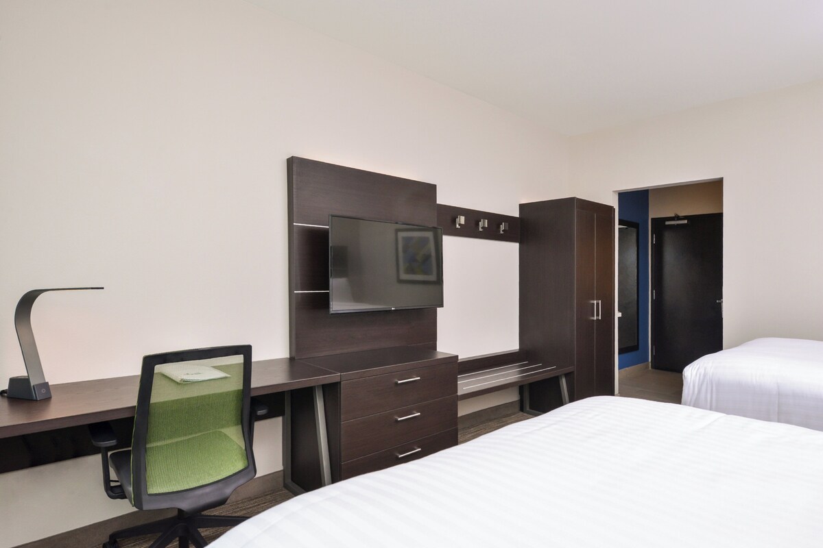 A hotel room with a desk, chair, television, wardrobe, and two beds.