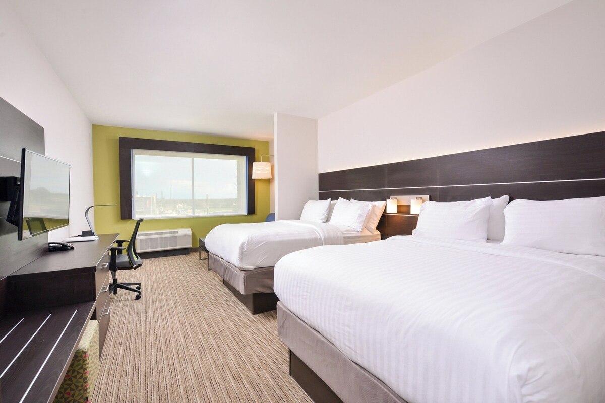 A hotel room with two beds, a desk, a TV, and a large window.