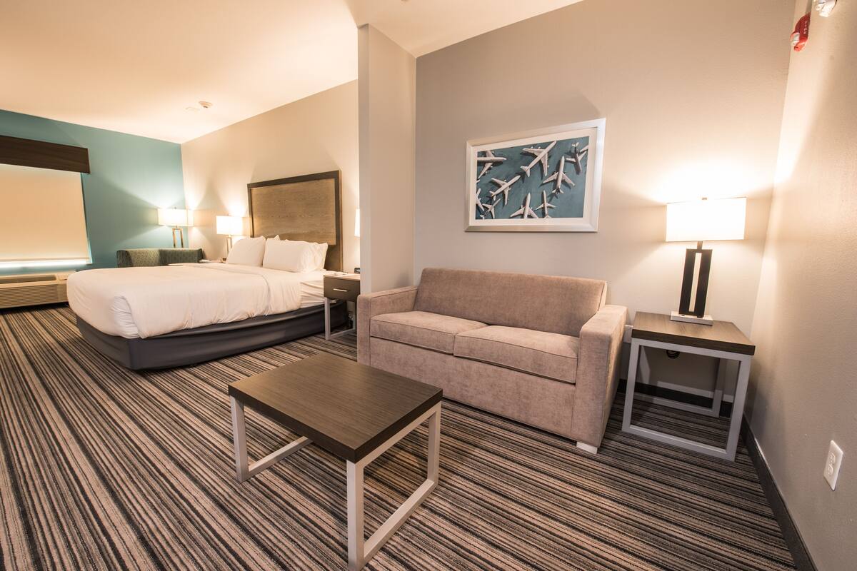 A hotel room with a bed, a sofa, a coffee table, and a painting on the wall.