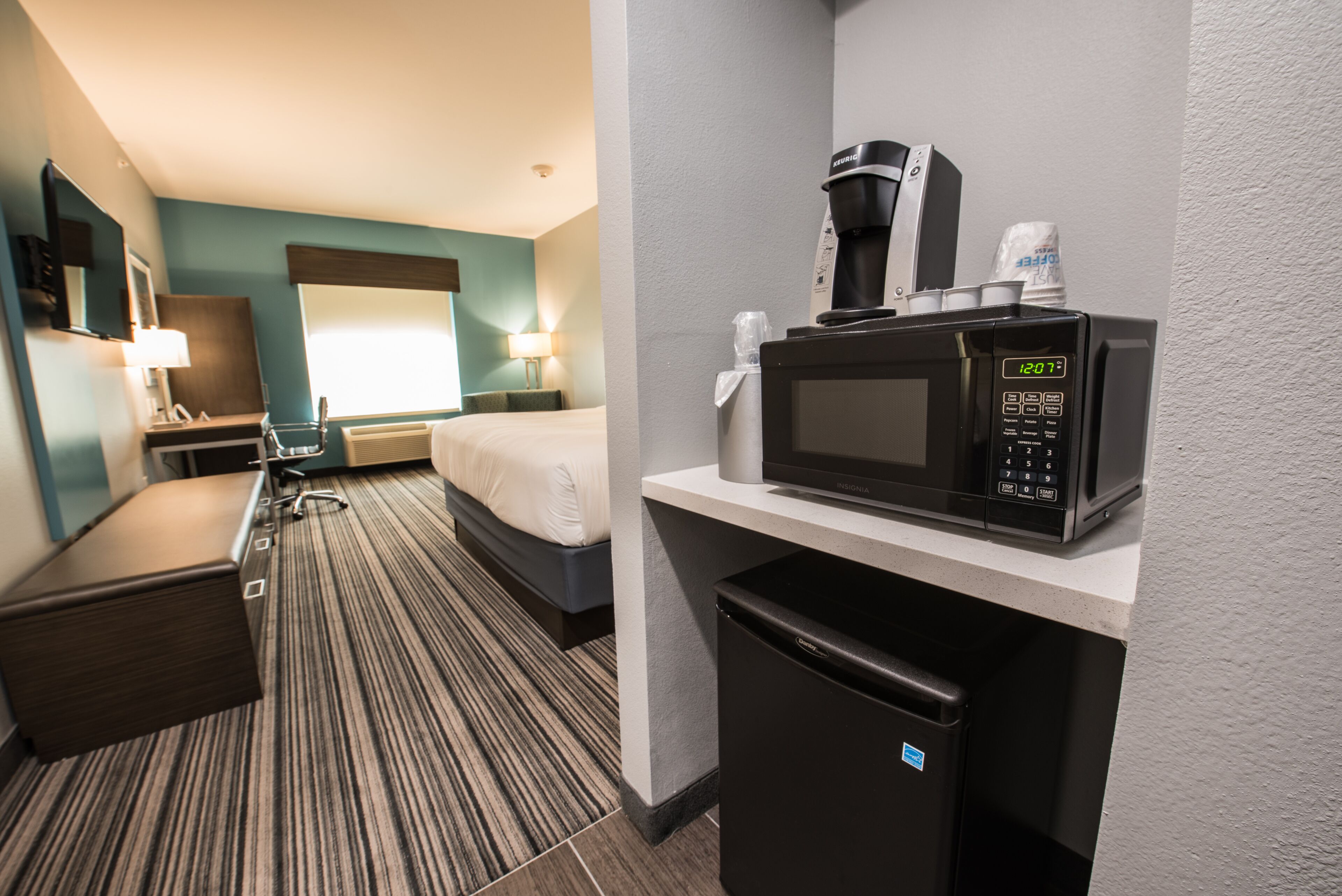 A hotel room with a bed, a desk with a microwave, a refrigerator, and a small cabinet.