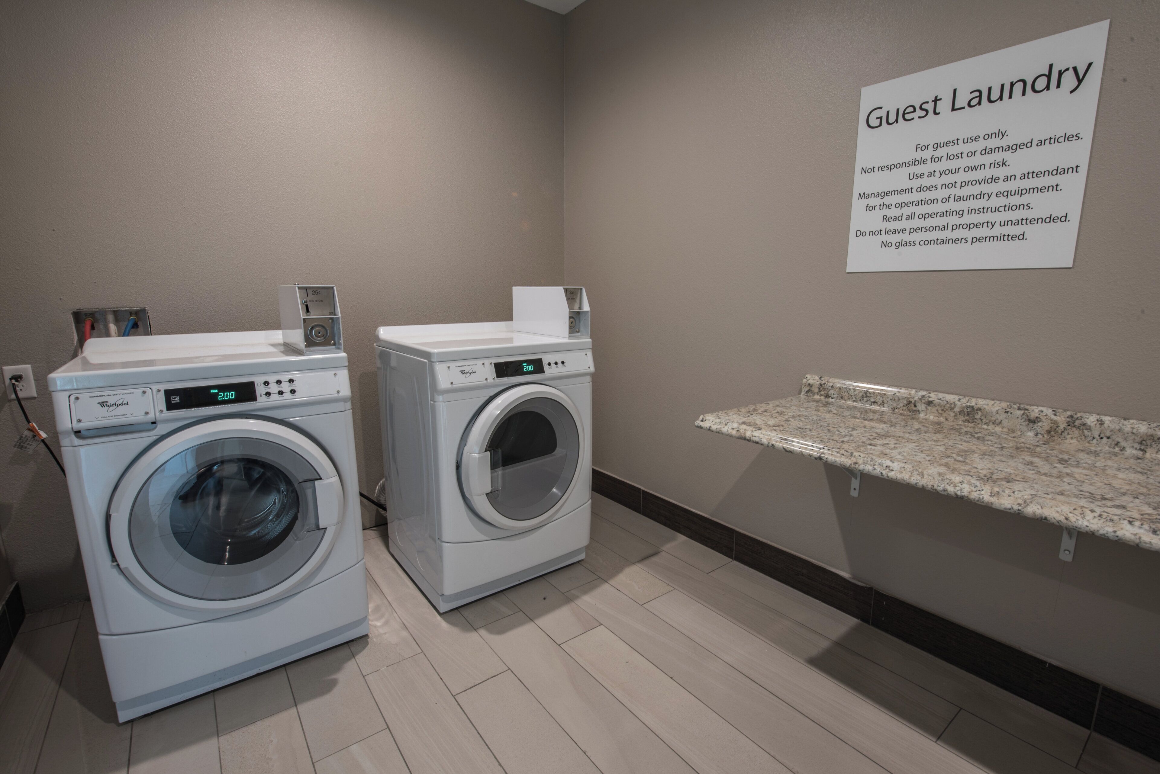 Un área de lavandería para huéspedes con dos lavadoras Whirlpool de carga frontal, un letrero con instrucciones de lavado y una encimera de granito.