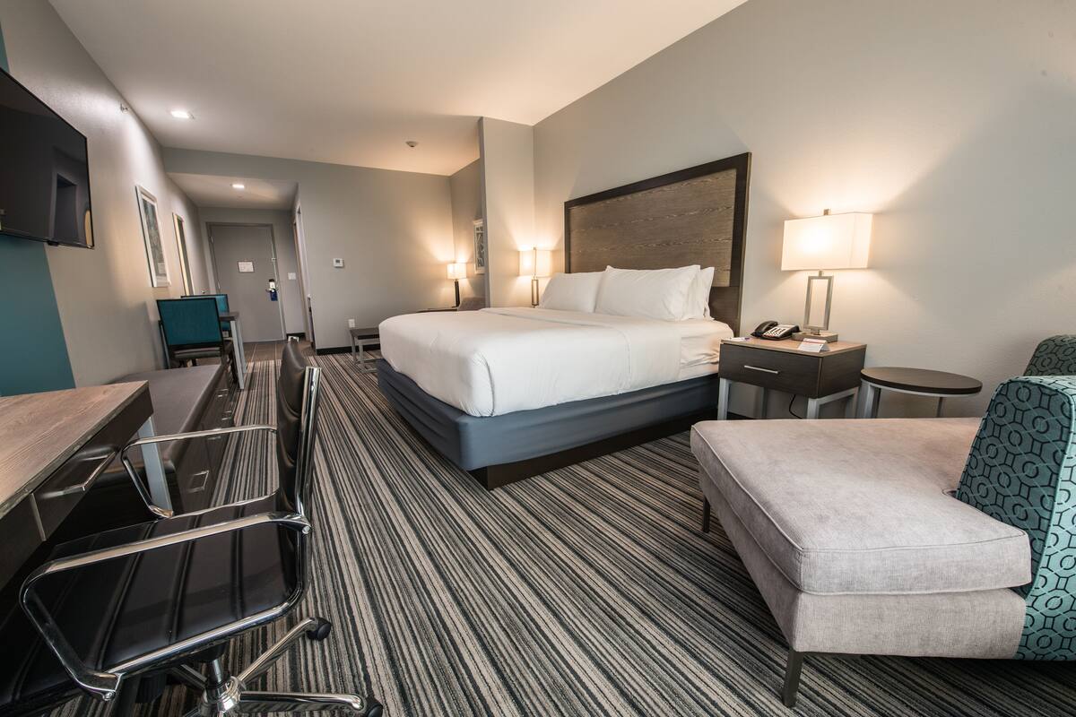 A hotel room with a large bed, a desk, a chair, a small table, and two bedside lamps.