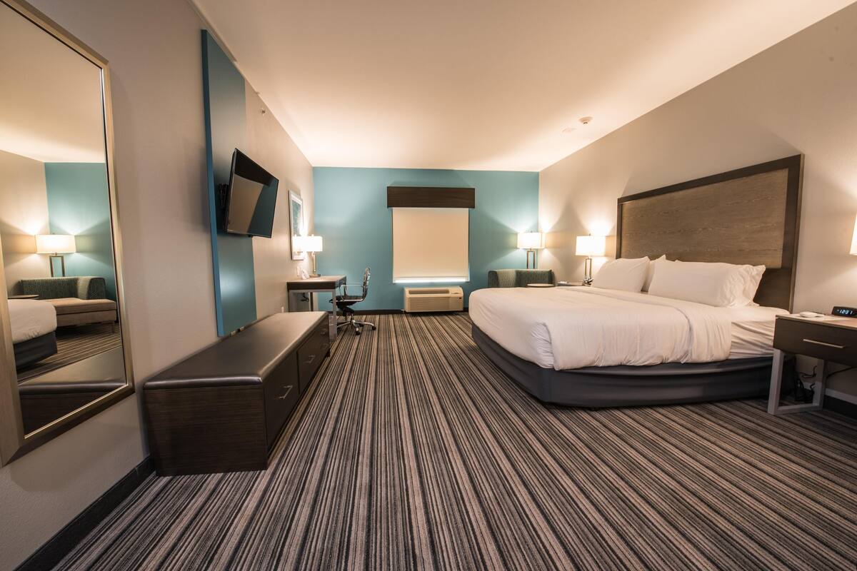 A hotel room with a large bed, a desk, a chair, a mirror, a TV, and a window.