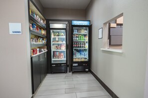 A hallway with two beverage vending machines, a sign labeled "SUNDRIES," and a small window with a view. - Holiday Inn Express & Suites Houston - Hobby Airport Area by IHG (Houston)