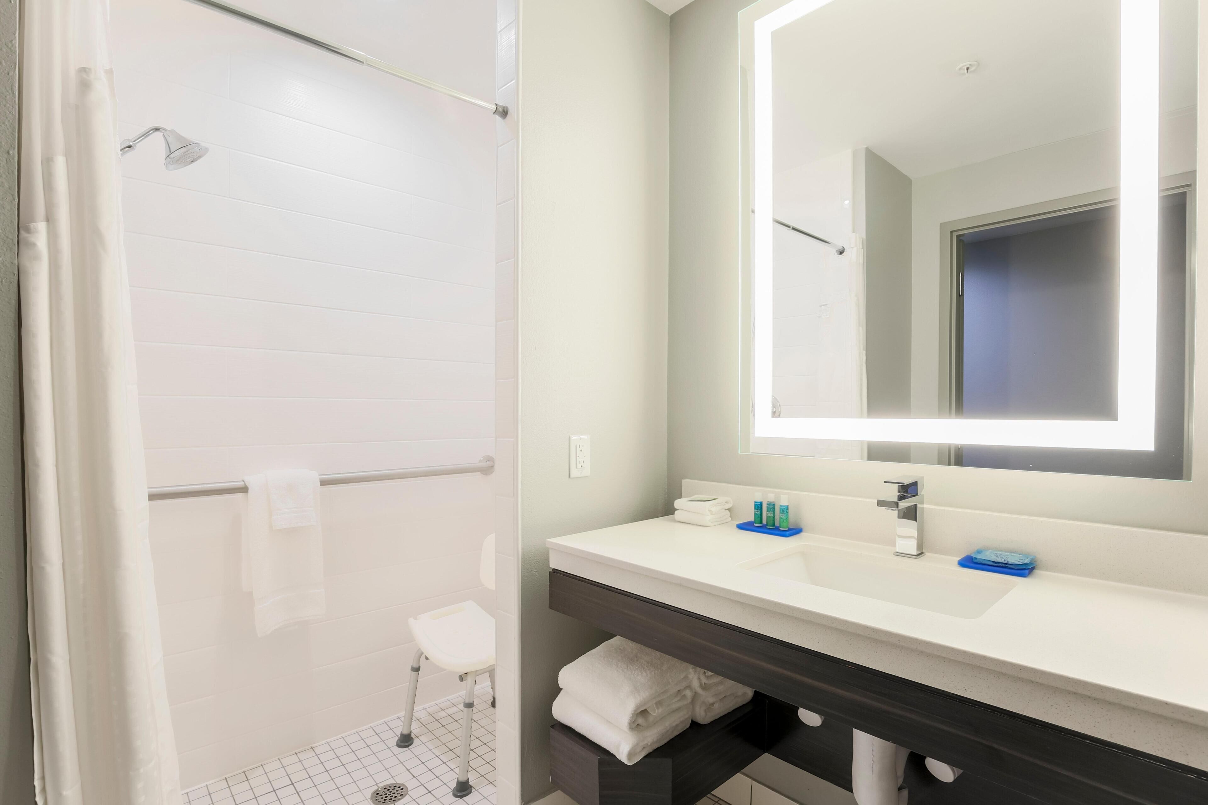 A modern bathroom with a shower, a white sink, a mirror, and a towel rack.