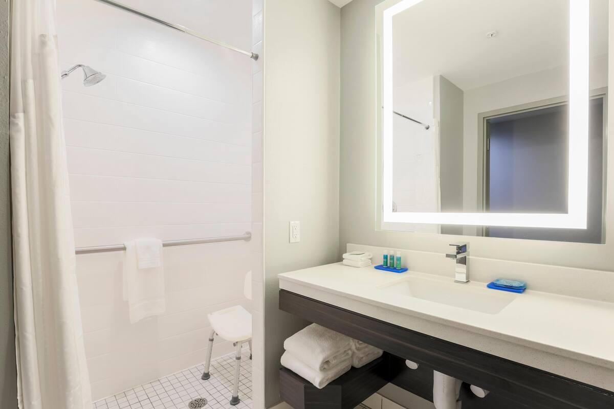 A modern bathroom with a shower, a white sink, a mirror, and a towel rack.