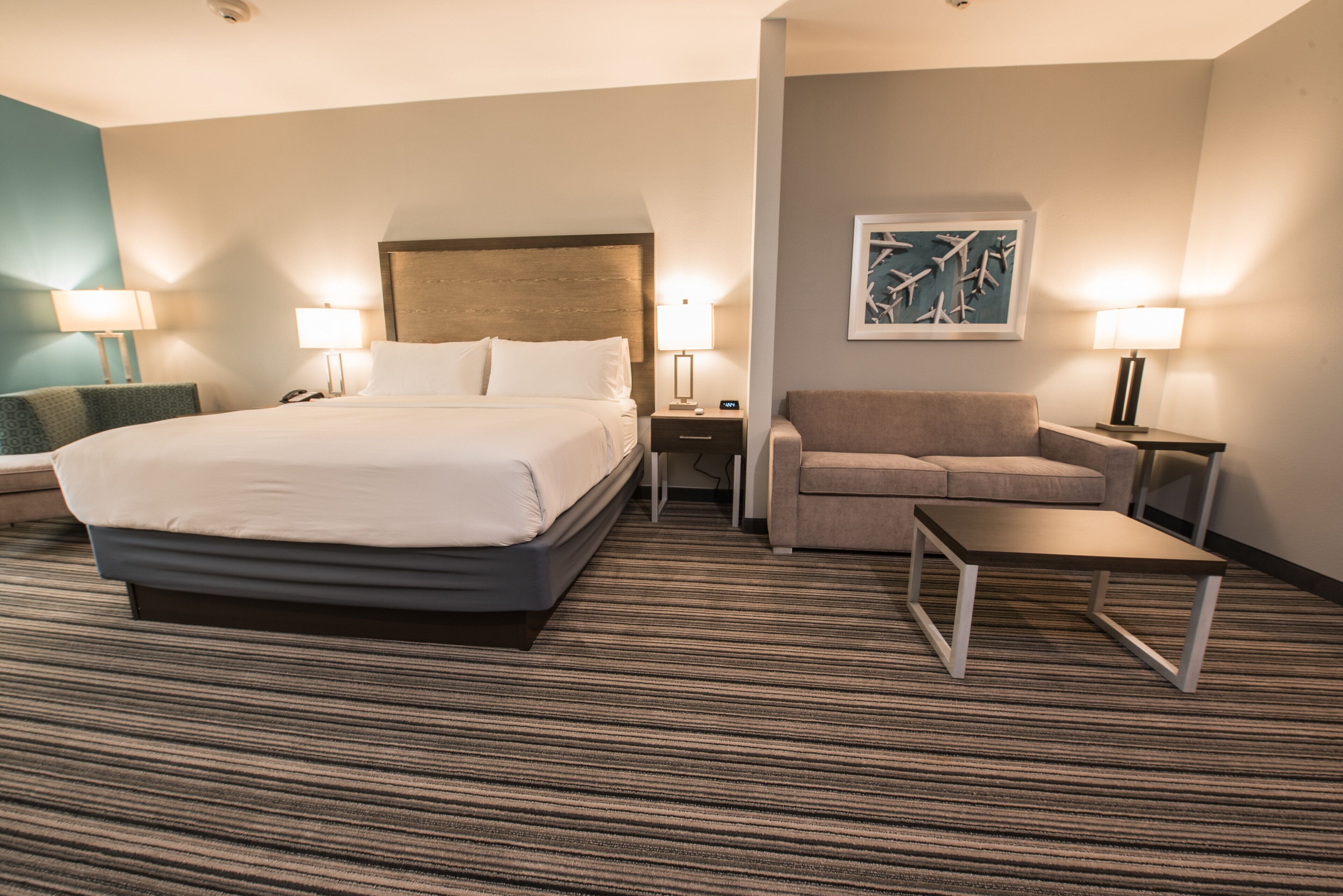 Una habitación de hotel con una cama grande, un sofá, una mesita y dos lámparas.