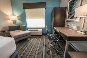 A hotel room with a bed, a desk, a chair, a lamp, a window with blinds, an air conditioner, and a wall-mounted artwork. - Holiday Inn Express & Suites Houston - Hobby Airport Area by IHG (Houston)