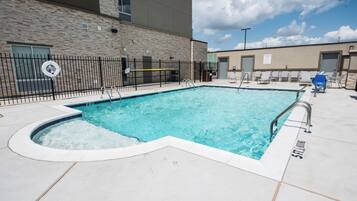 Ein rechteckiger Pool mit gewölbtem Abschnitt, umgeben von einer gefliesten Poolterrasse.