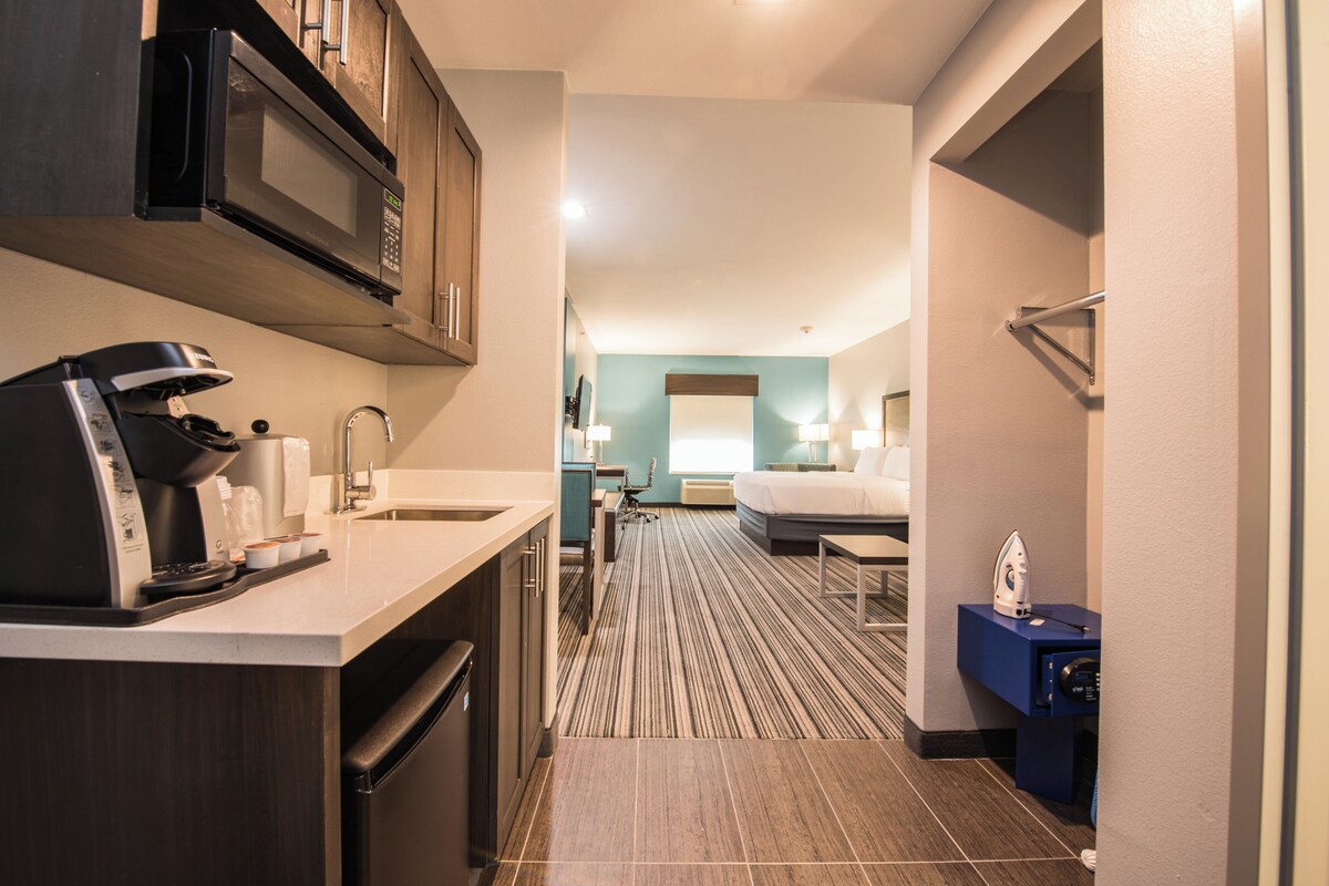 A hotel room with a kitchenette, a bed, and a bathroom.
