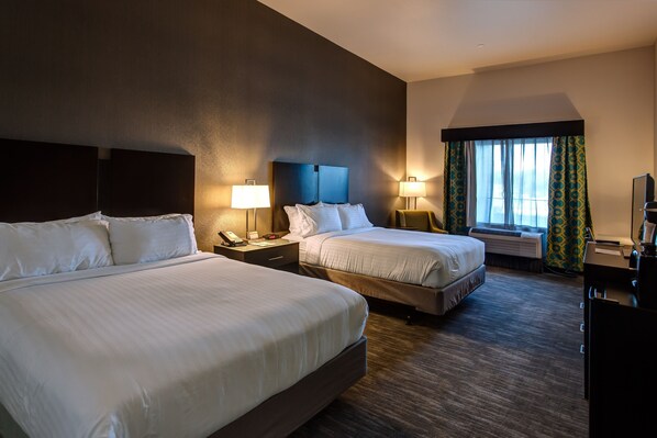 Een hotelkamer met twee bedden, een bureau, een stoel, een televisie en een raam met gordijnen.