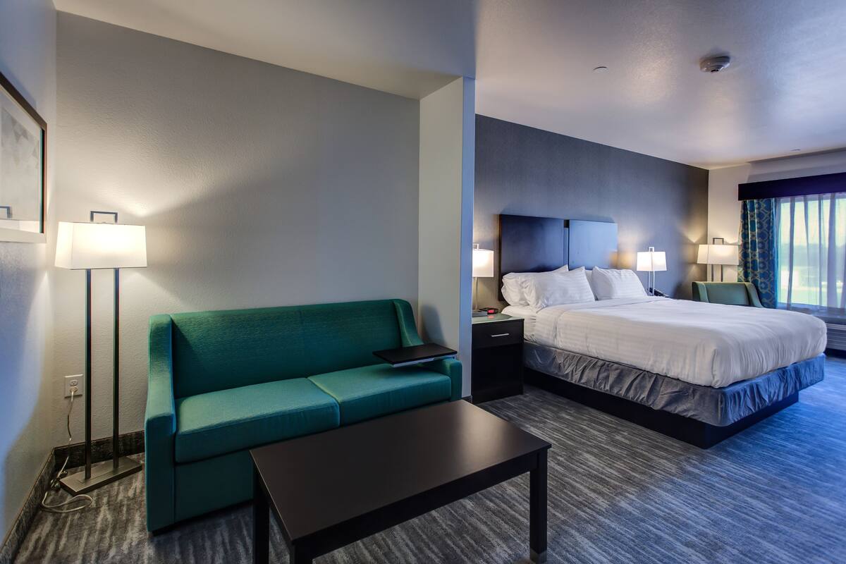 A hotel room with a bed, a green sofa, a small table, and a nightstand with a lamp.